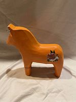 Side view of the orange wooden Dala horse with floral decorations and metal ring on nose.