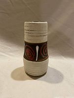 Front view of the West Germany Mid Century pottery vase showing textured off-white top and bottom with brown band featuring red spirals and white linear motifs.