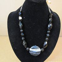 Full view of the necklace displayed on black stand showing the faceted black onyx beads and the large faceted agate centerpiece with white and gray banding.