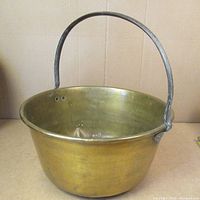 Full view of antique brass cooking pot showing round shape and iron handle.