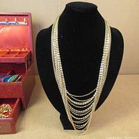 Full view of gold-tone chains on black stand and red jewelry box with compartments open showing assorted jewelry pieces inside.