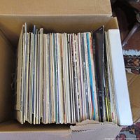 Top-down view of a box packed with assorted LP vinyl records showing their spines and edges.