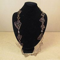 Full view of the copper costume jewelry necklace displayed on a black bust stand showing the linked open triangle copper wire shapes with spiral design.