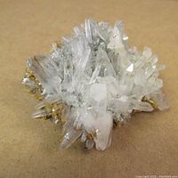 Close-up front view of transparent prismatic crystal cluster on brownish base showing sharp crystal terminations and mineral growth.