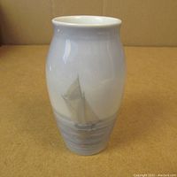 Photo of porcelain vase showing sailing boat design on front with smooth, glossy finish and soft blue-gray tones.