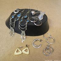 Overview of multiple pairs of silver and cream colored earrings arranged on a display surface, including long dangles with blue enamel and hoop styles, showing wear consistent with vintage condition.