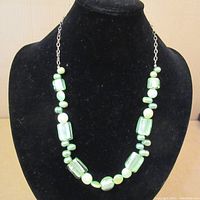 Full view of the necklace displayed on a black bust showing green foiled glass rectangular beads alternated with smaller round green beads and green pearls on a sterling silver chain.