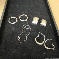 Four pairs of sterling silver earrings displayed on black fabric background in a box.