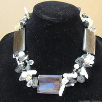 Front view of the handmade stone necklace on a black display stand showing central rectangular polished stones and clusters of various stones and pearls.