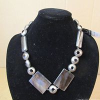 Full view of the necklace on a black velvet display stand, showing rectangular stone beads and black rhodium plated copper beads in various shapes including round and tubular.