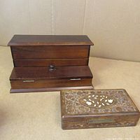 Wooden desk organizer with pull-out drawer and knob beside rectangular wooden trinket box with carved details, both shown on cardboard background.