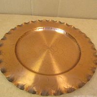 Top-down photo showing the large round copper dish with scalloped edges and hammered decorative patterns etched on surface.