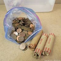 Loosely sorted Canadian penny coins in resealable plastic bag with three rolls of Canadian pennies in red and beige paper coin wrappers.