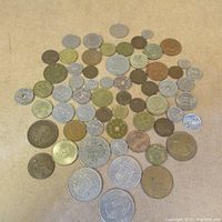 Full view of 48 assorted world coins laid out on a beige surface, varying in size, color, and metal composition, some with holes in the center.