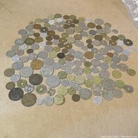 Wide-angle photo showing a large collection of diverse coins spread out on a flat surface, revealing differences in size, color, and shape.
