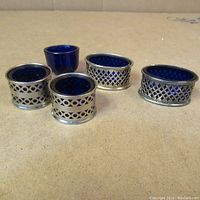 Five open salt cellars with cobalt blue glass inserts on a flat surface, showing overall lot composition and condition.