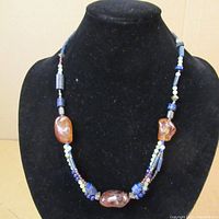 Front view of the full necklace displayed on a black velvet stand showing assorted beads and stones with the sterling silver clasp not visible