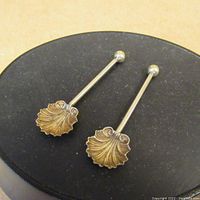 Pair of vintage continental silver salt spoons displayed on a black cylindrical stand, showing shell-shaped decorative bowls and ball-end handles.