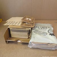 Image showing an open box containing a stack of flat brown paper Electrolux vacuum bags alongside a sealed white package labeled 'Electrolux 12 Bags.'