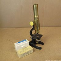 Photo showing antique brass microscope, black base, and two boxes of vintage glass slides in front.