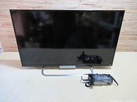 Full front view of Sony 32 inch flat screen TV on stand with power adapter on floor in front.