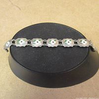 Full view of the sterling silver dogwood bracelet showing linked enameled floral panels on display stand.