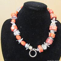 Necklace with coral-colored barrel stones alternating with clear quartz-like stone chunks and silver spacers on black display stand