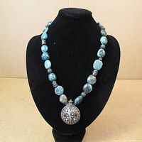 Full view of the necklace displayed on a black bust showing turquoise stones and central pendant.