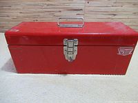 Closed view of red metal toolbox with handle and latch, showing International SPG logo.