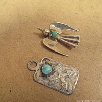 Two Mexican silver pendants on brown background; bird shaped with turquoise and rectangular with cross and arrows design and turquoise