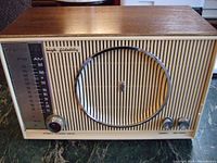 Front view of Zenith radio showing teak cabinet, vertical slat grill, chrome circular speaker surround and controls with AM/FM tuning scale.