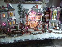Full front view of the fiber-optic lit Christmas village scene with houses, trees, and figurines on snowy base.