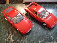 Top view of two red diecast Ferrari models on green marble surface showing exterior features and proportions