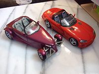 Two diecast model cars including metallic burgundy Plymouth Prowler concept and bright red Dodge Viper RT/10 convertible on marble countertop
