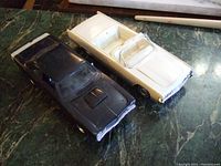 Top view of black Dodge Super Bee and white Lincoln convertible model cars on a green marble surface