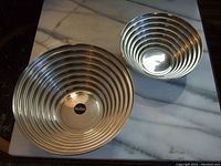 Two nested salad bowls showing their concentric ribbed design and polished stainless steel surface on a marble table.