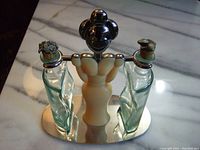 Full view of the Bugatti condiment set showing stainless steel base, plastic central figure handle, and two curved glass bottles with metal stoppers.