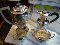 Full view of coffee pot, tea pot, creamer, and sugar bowl arranged on marble surface, showing overall design and condition.