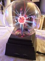 Clear plasma globe showing colorful plasma filament sparks inside glass sphere on black base with intensity control slider and power switch.