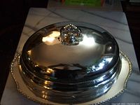 Overall view of silver turkey platter with large domed cover, shiny metal reflecting surroundings.