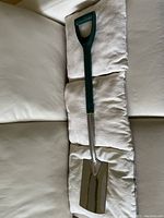 Full view of silver plated shovel with green rubber handle placed on cushions