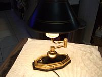 Small black toleware swing arm desk lamp on white cloth background, showing lamp base and shade with gold accents.