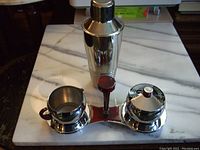 Full view of the cocktail shaker and the cream and sugar set on stand showing design and finish.