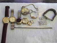 All eight watches and jewelry components displayed on white cloth. Includes wristwatches with bands, pocket watch, chain bracelet, and bags of silver jewelry parts.