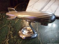 Side angle showing the entire aluminum zeppelin blimp and its smooth shiny stand on a marble surface.