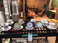 Overview of ten bone china teacups and nine saucers arranged on plastic shelving grid