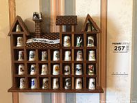 Full view of the wooden thimble display shelf with 28 bone china thimbles neatly arranged in individual compartments shaped as a house with roof and chimneys.