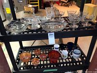 Two shelf display of assorted dishware including glass, crystal, carnival glass and ceramic cups and bowls, total 23 pieces visible
