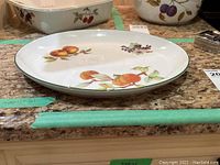 Oval ceramic platter with hand-painted fruit including peaches and grapes on white background.