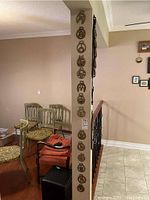 Photo showing fourteen horse brasses mounted vertically on a wall or pillar, various horse and horseshoe designs visible.